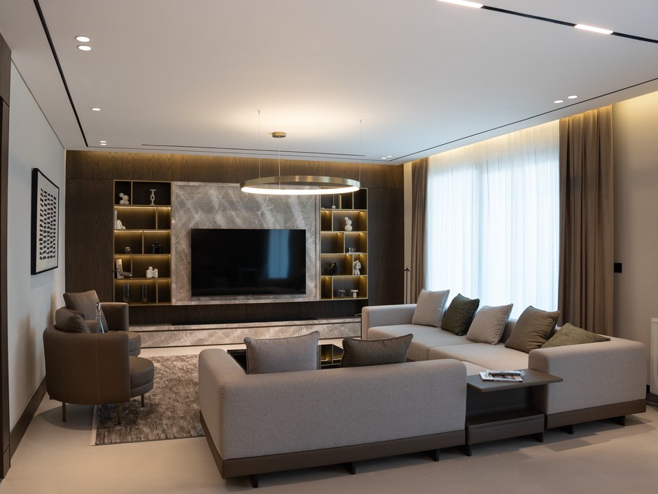 Contemporary lounge with a neutral sectional sofa, warm wood accent wall and a round gold pendant light